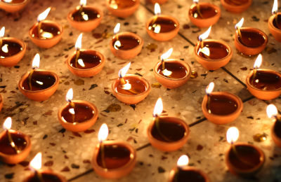 Numerous small clay lamps with flickering flames arranged closely on a speckled surface, emitting a warm, golden light.