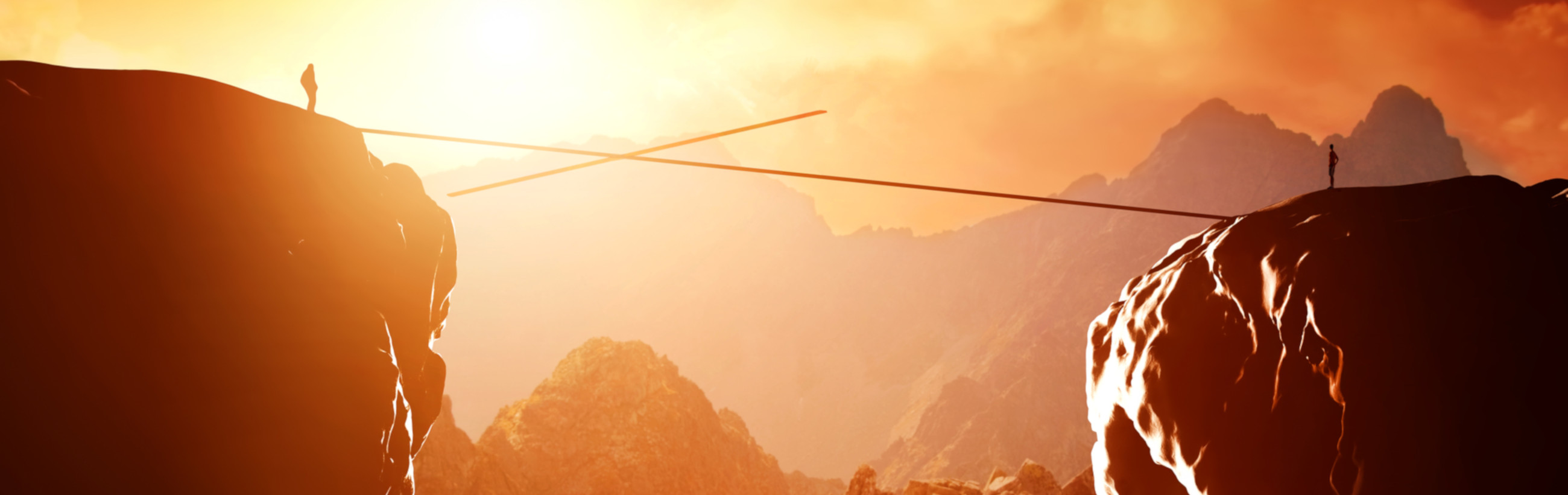 A panoramic view of two silhouetted figures standing on distant rocky peaks, connected by a tightrope beneath an orange-hued sky, symbolizing balance and challenge amidst the grandeur of creation.