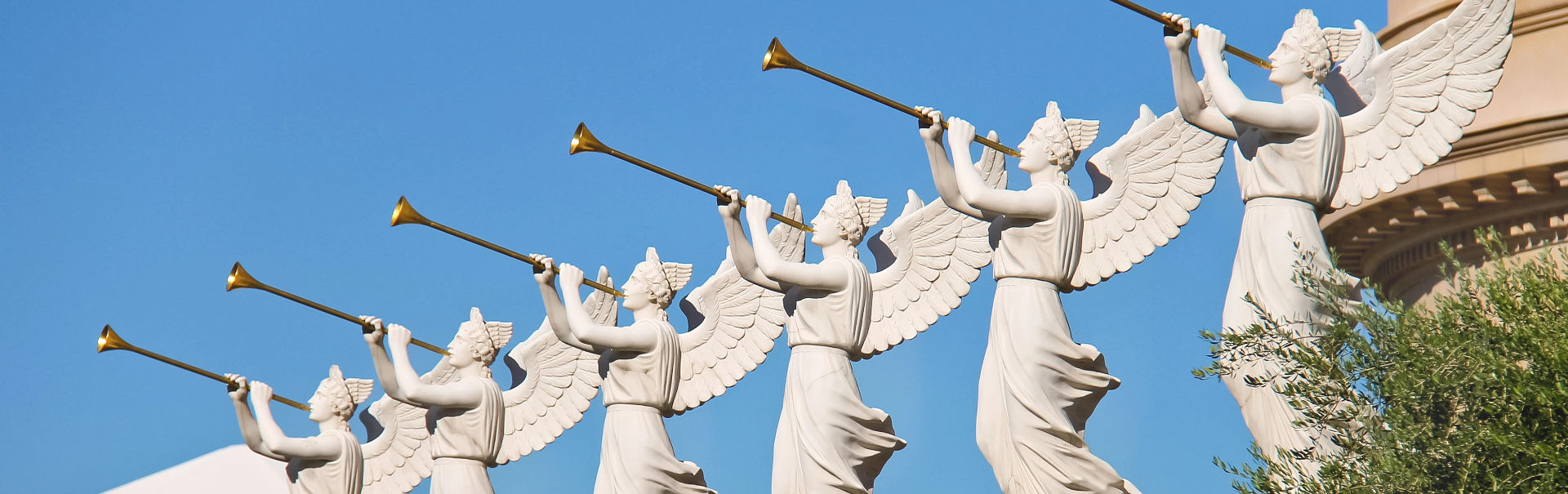 A row of five statues of celestial messengers, each depicted with wings and trumpets, positioned against a clear blue sky. These sculptures portray messengers that could be likened to the heralds of the Mazzaroth, each wearing flowing robes and sounding their trumpets towards the heavens.