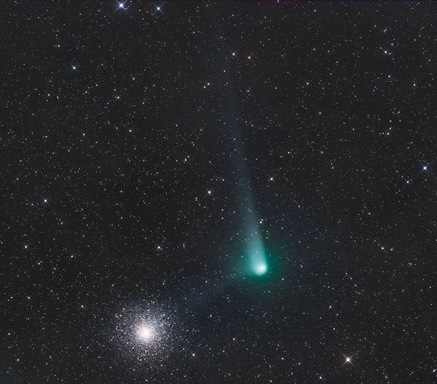 A celestial image featuring a bright comet with a luminous turquoise-hued nucleus and an extensive tail, traveling through a densely star-packed region of space. Near the comet, a brilliant cluster of stars adds a sparkling contrast to the deep black cosmos.